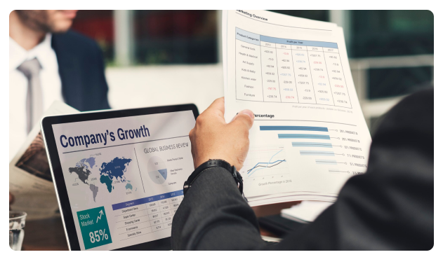 Businessman holding a tablet showing 'Company's Growth' beside printed reports and charts
